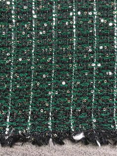 a close up view of the green and black fabric with white beads on it's edges