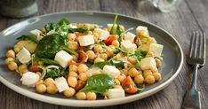 a white plate topped with chickpeas, spinach and feta cheese on top of a wooden table