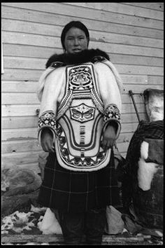 an old black and white photo of a woman in traditional clothing standing next to a building