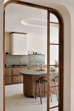 a kitchen with an oval table and stools in front of the counter top is seen through a doorway