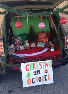 the back of a van with christmas decorations and presents in it's trunk, next to a sign that says christmas in october