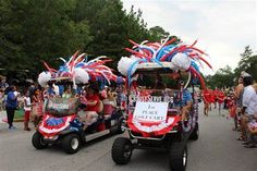 some people are riding in a golf cart with flags and balloons on the side walk