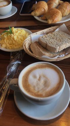 there is a cup of coffee, bread and other food on the table in front of it