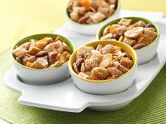 three bowls filled with chex mix sitting on top of a white tray