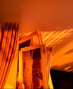 a stack of framed photographs sitting on top of a table next to a window covered in blinds