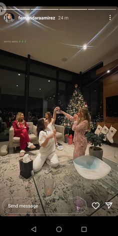 two people are sitting on the floor in front of a christmas tree and one person is taking a selfie