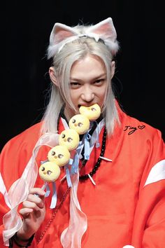 a woman in an orange jacket eating some food with her eyes closed and cat ears sticking out