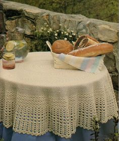 a crochet tablecloth with bread and drinks on it sitting on top of a stone wall