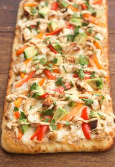 a long rectangular pizza with vegetables and meat toppings on it's edges, sitting on a wooden surface