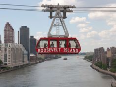 a red cable car with people on it going over the river in roosevelt island