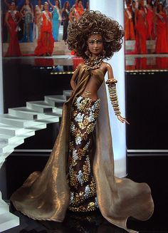 a barbie doll wearing a gold and white dress with an elaborate headpiece on display