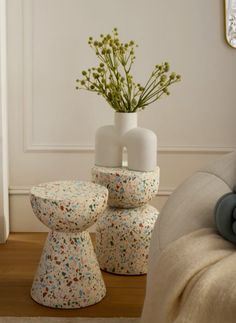 three white vases with flowers in them sitting on a wooden floor next to a couch