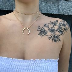 a woman with a tattoo on her chest wearing a white tank top and gold necklace