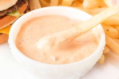 a close up of a sandwich and french fries on a white plate with a dipping sauce