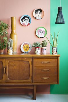 there are many plates and plants on the sideboard in this living room with pink walls