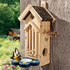 a wooden bird house hanging on the side of a tree with butterflies flying around it