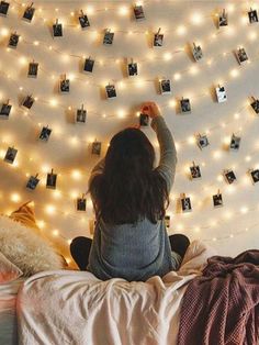 a woman sitting on top of a bed next to a wall covered in pictures and lights