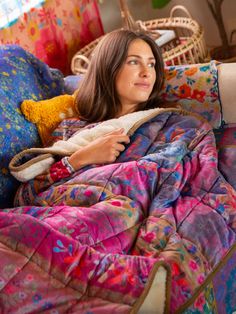 a woman laying on top of a bed covered in a colorful comforter and blanket