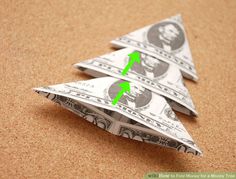 two origami christmas trees made out of one dollar bill with an arrow pointing to the other