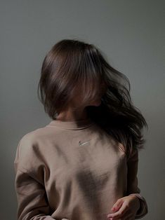 a woman with long hair standing in front of a white wall wearing a brown sweatshirt