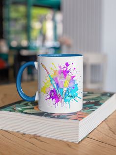 a coffee mug sitting on top of a book with paint splatters all over it