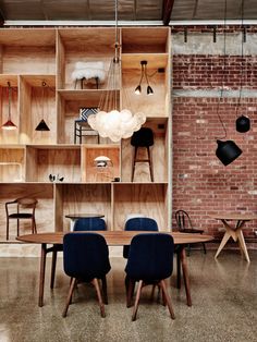 a room filled with lots of wooden shelves and chairs next to a dining table in front of a brick wall