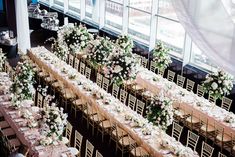 an overhead view of tables and chairs in a room with tall windows, decorated with white flowers