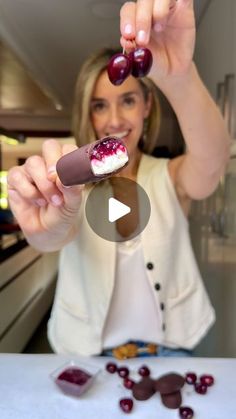 a woman is holding up a chocolate covered pastry with cherries on it and she is about to eat the cake