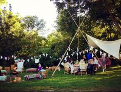 a group of people sitting around a table in the grass under a tent with clothes hanging from it