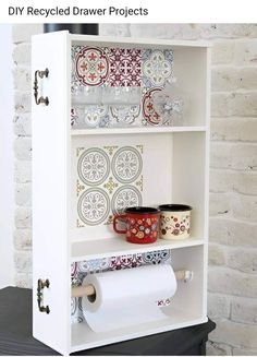 a white book shelf with some plates and cups on it next to a brick wall