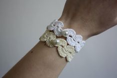 a woman's arm wearing a white and beige crochet bracelet with pearls