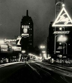 a black and white photo of a city street at night with tall buildings in the background