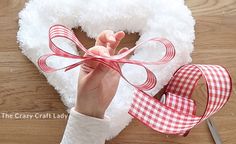 a person is holding up a heart shaped wreath with ribbon on it and scissors next to it