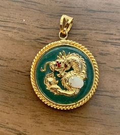 This is a vintage jade pendant. The dragon, rim, and bail are gold tone. The dragon has a red rhinestone eye and is holding an opal egg. It is approximately 1 inch in diameter. There are some small imperfections on the back due to its age. There is no chain. Red Rhinestone, Pendant Gold, Jade Pendant, The Dragon, Gold Pendant, Pendant Necklaces, Jewelry Necklace Pendant, 1 Inch, Jade