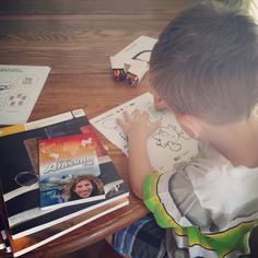 a young boy is sitting at a table with books and crayons on it