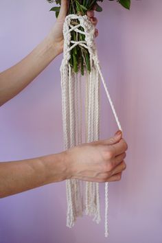 two hands holding flowers that have been tied to the wall with string and rope hanging from them