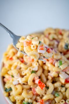 a spoon full of macaroni and cheese with colorful toppings in a bowl