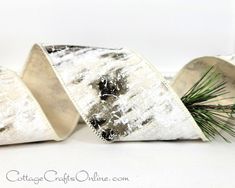 two silver and white napkins sitting on top of each other next to a pine branch