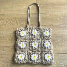 a crocheted bag with white and yellow flowers on the front, sitting on a wooden floor