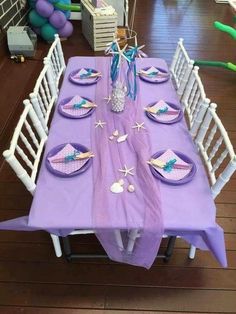 the table is set with purple and white plates, napkins and place settings for an ocean themed party