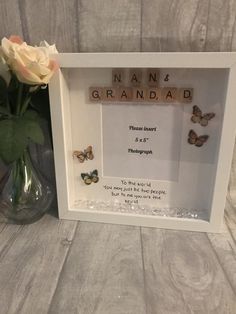 a white frame with three butterflies and a vase filled with flowers on top of a wooden table