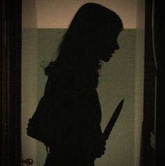 the silhouette of a woman holding a knife in front of a door with light coming through it