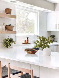 a white kitchen with wooden chairs and plants on the counter