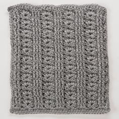 a gray crocheted square on top of a white surface with the corner stitched in