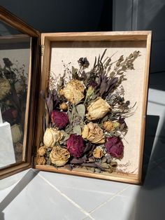 two framed pictures with dried flowers in them on a white counter top next to each other