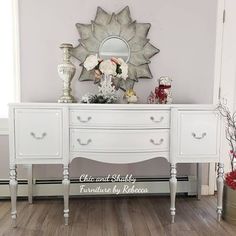 a white dresser sitting on top of a hard wood floor next to a mirror and vase