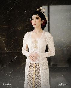 a woman in a white dress standing next to a marble wall with her hands on her hips