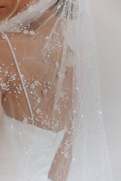 a woman wearing a wedding veil with pearls on it's head and neckline