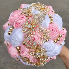 a bridal bouquet with pink roses and gold brooches is being held by someone's hand