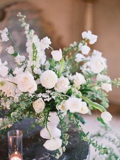 white flowers and greenery in a vase on a black table with two lit candles